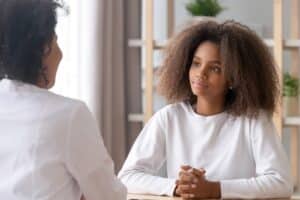 Focus on african adolescent teen girl listening medical worker her psychotherapist, therapist counsellor or pediatrician while visiting doctors office. Teen problems, therapy session medicine concept